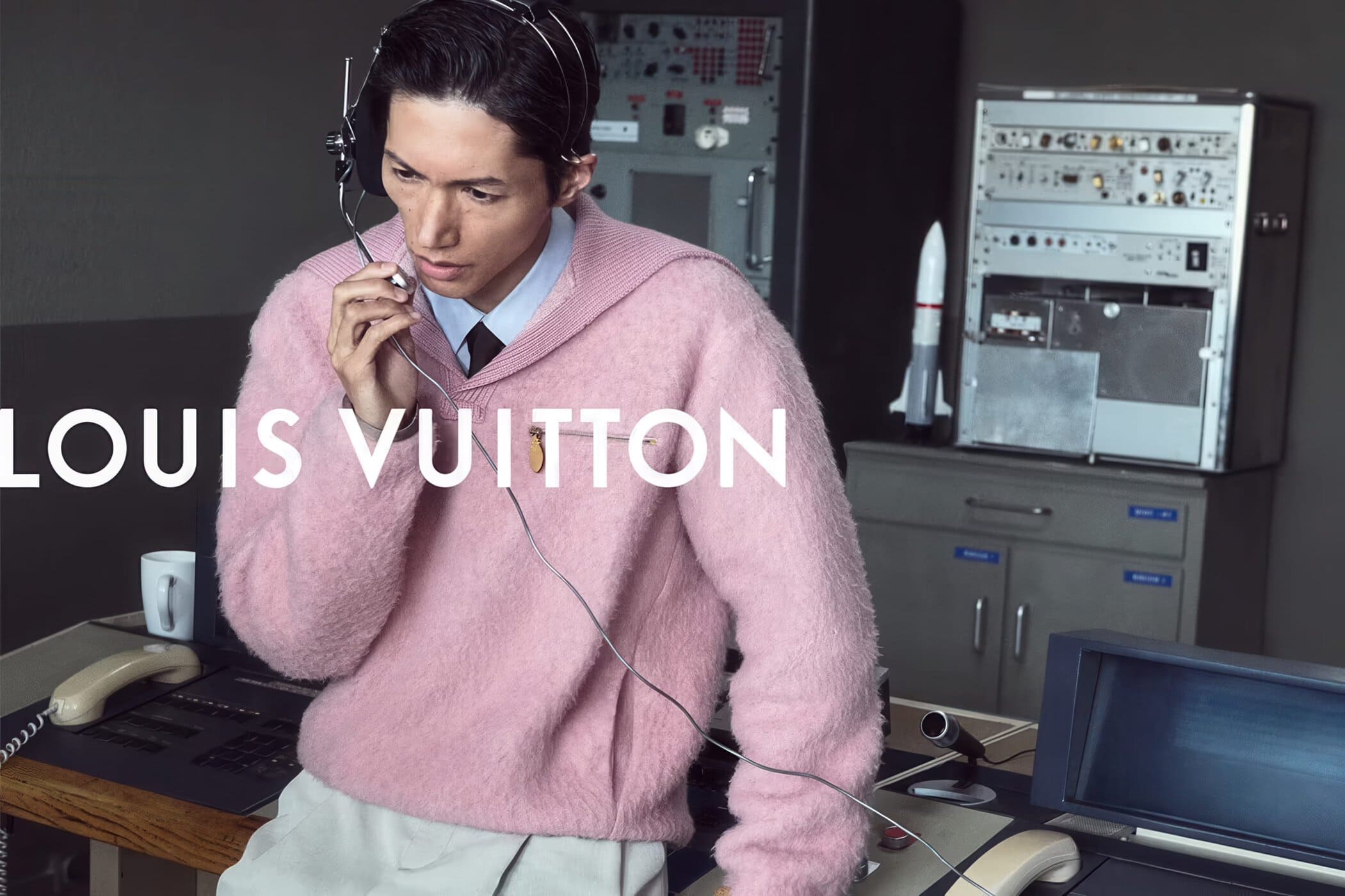 Model Takahiro Oda wearing a pink knit sweater and vintage communications headset at a control desk in a Louis Vuitton campaign.