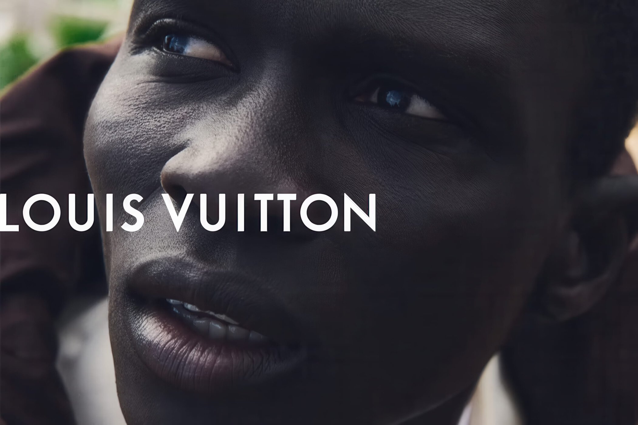 Close-up portrait of a Black man looking upward with white Louis Vuitton typography overlay across his face.