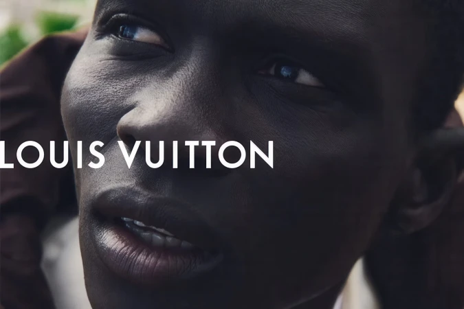 Close-up portrait of a Black man looking upward with white Louis Vuitton typography overlay across his face.