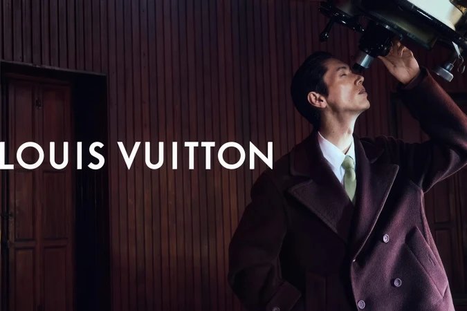 Man in a dark burgundy wool coat and tie looking through an astronomical telescope in a wood-paneled room.