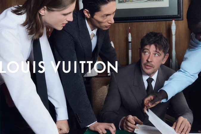 Men dressed in tailored suits and collared dress shirts gathering around a desk to review documents in an office.