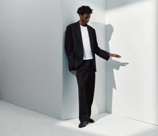 Model Ahmed Richards in an oversized black suit and white t-shirt posing against white minimalist geometric walls.