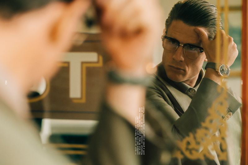 James Norton wearing horn-rimmed eyeglasses and a tailored jacket reflected in a mirror.