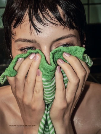 Close-up portrait of a woman with short wet dark hair holding a green and white striped towel over her face.