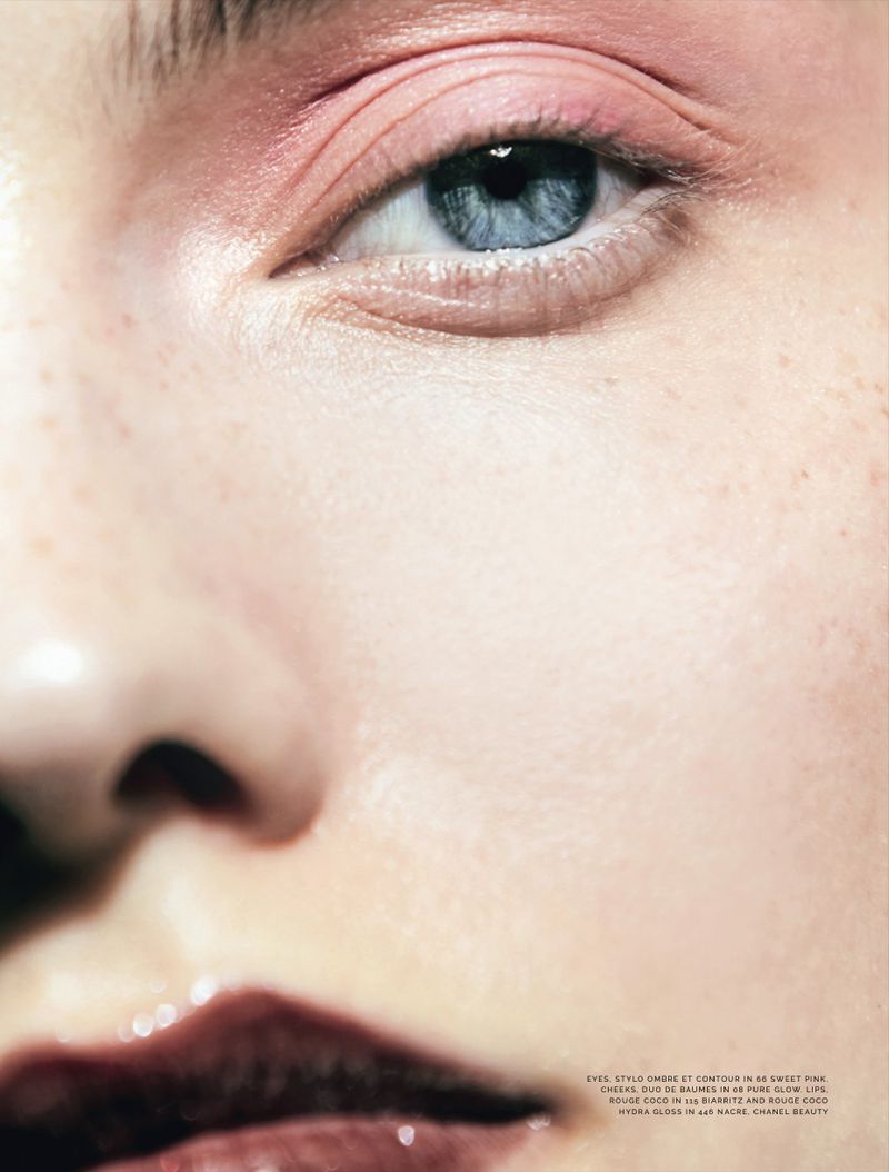 Extreme close-up beauty portrait of a woman with a blue eye, soft pink eyeshadow, and glossy dark berry lips.