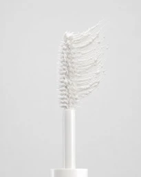 Close-up of a white mascara wand with thick textured white cosmetic paste swiped against a seamless off-white background.