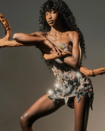 Model Rosario Saidi poses with a wooden branch wearing an embellished cutout mini dress against a neutral studio backdrop.