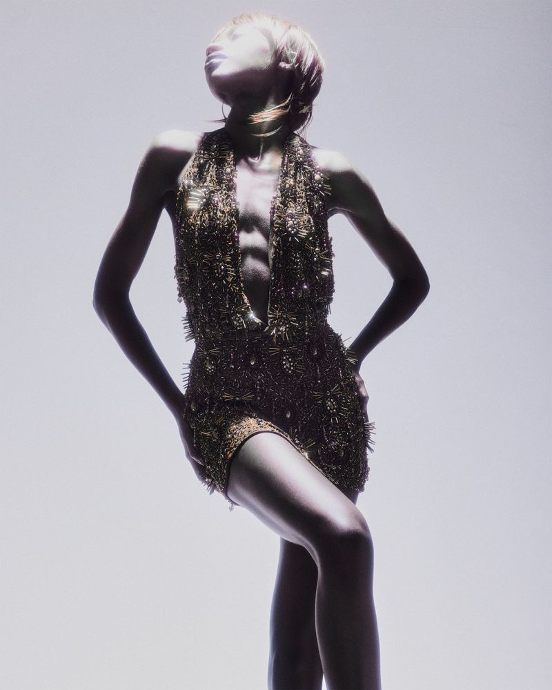 Model Rosario Saidi posing in a textured metallic halter minidress against an illuminated pale studio backdrop.
