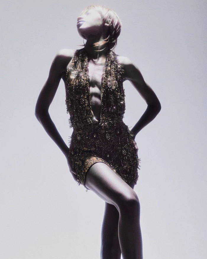Model Rosario Saidi posing in a textured metallic halter minidress against an illuminated pale studio backdrop.
