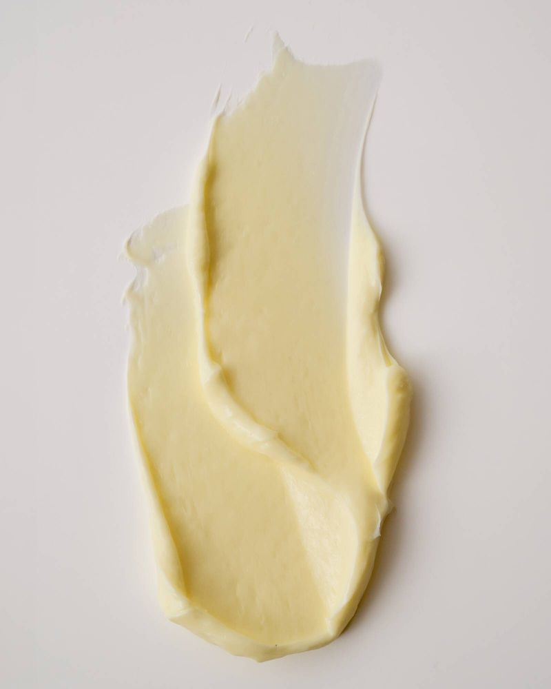 Textural swatch of pale yellow cosmetic cream smeared smoothly across a neutral off-white surface.