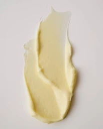Textural swatch of pale yellow cosmetic cream smeared smoothly across a neutral off-white surface.