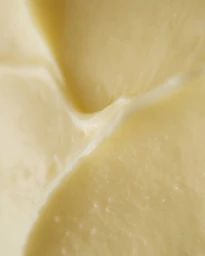 Macro close-up photograph of creamy pale yellow skincare product showing smooth, buttery texture and soft ridges.