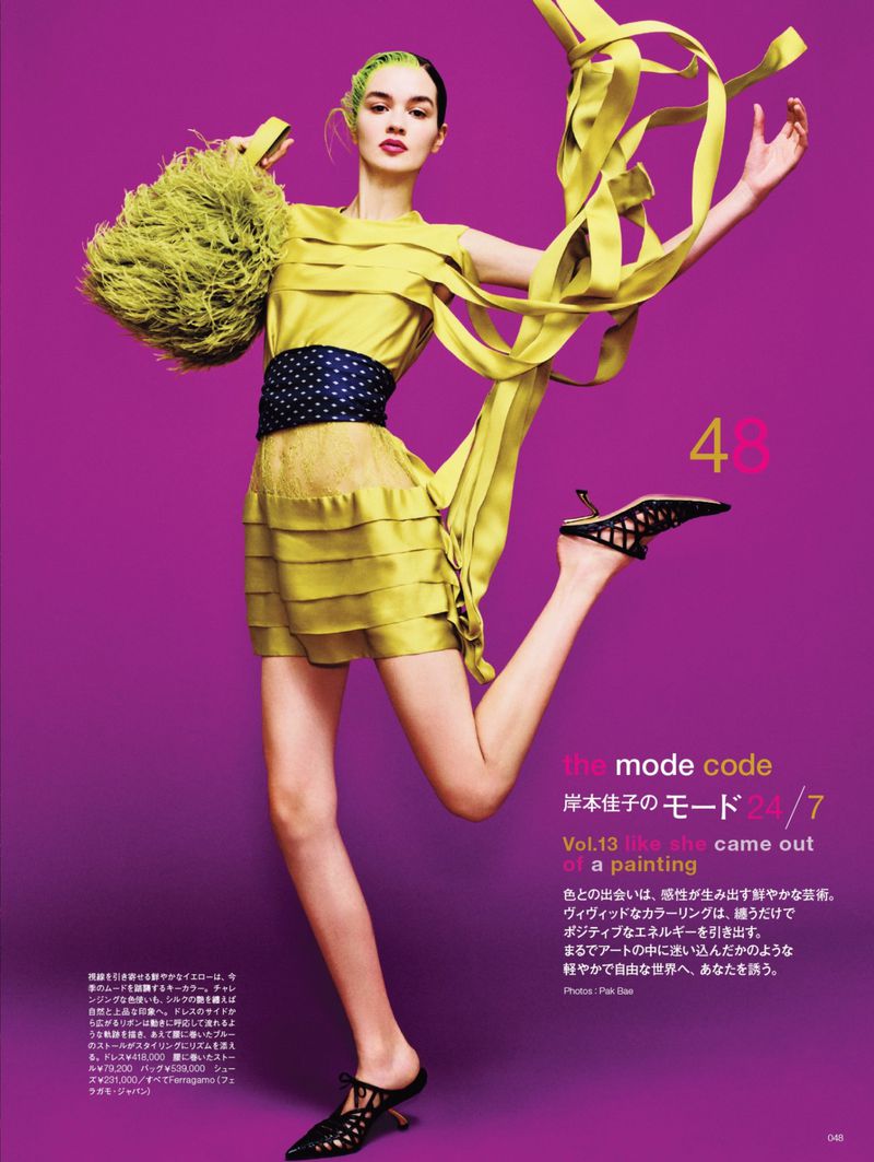 Model jumping in yellow dress with ribbons and feathered handbag against solid magenta background for Numero Tokyo