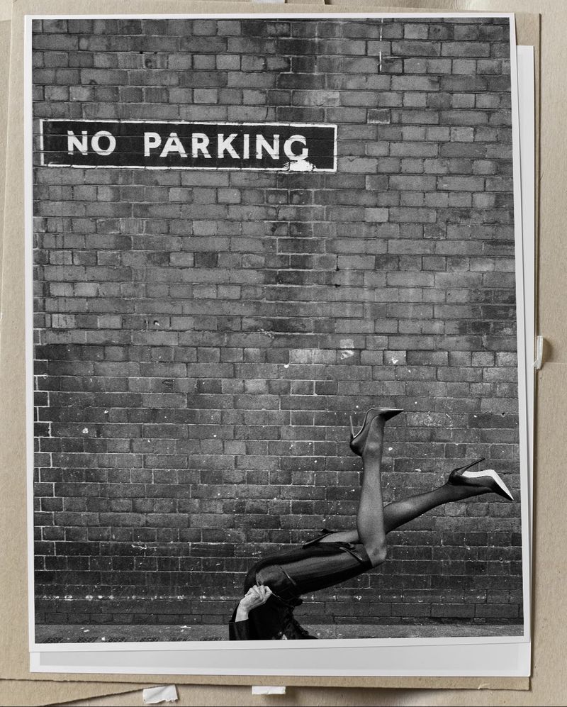 Black and white photo of model Georgia Palmer posed upside down in high heels against a brick wall below a No Parking sign.