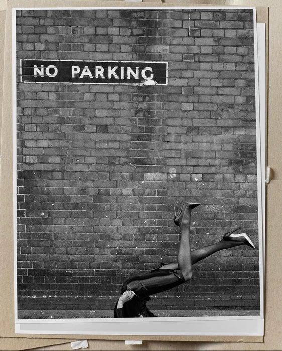 Black and white photo of model Georgia Palmer posed upside down in high heels against a brick wall below a No Parking sign.