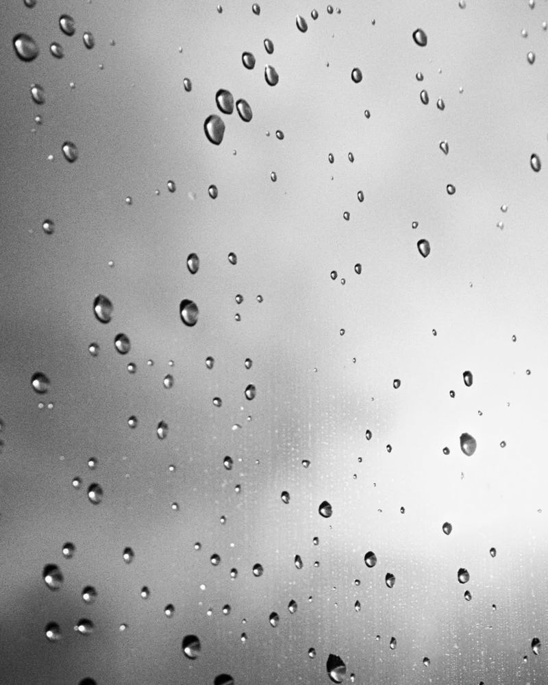 Monochrome close-up of water droplets scattered across a glass surface against a soft light background.