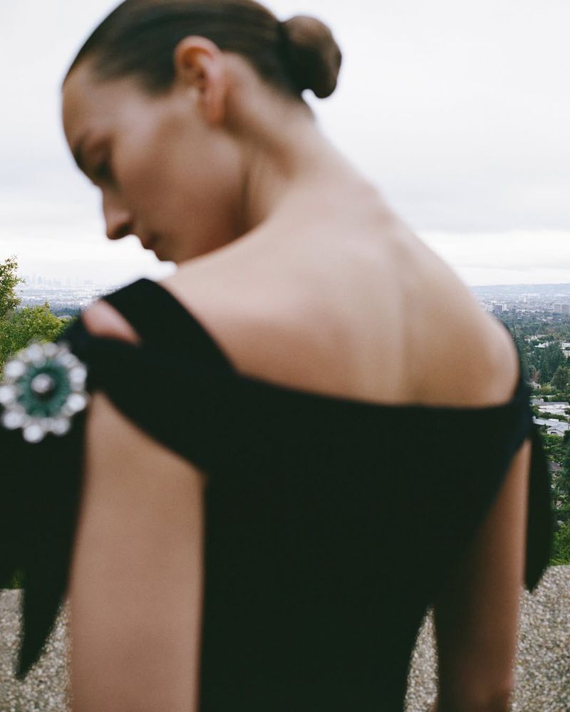 Model Julia Bergshoeff seen from behind wearing an off-the-shoulder black dress with an ornate green jewel brooch for Wallpaper Magazine.