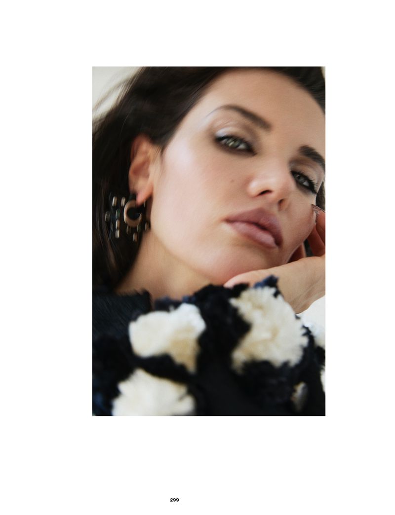 Close-up portrait of a woman wearing a black-and-white textured floral garment and large earring, resting her head on her hand.