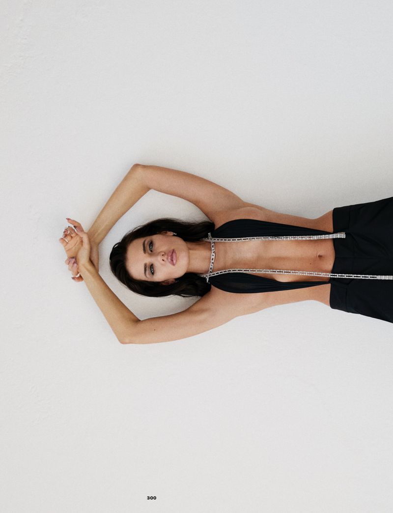 Fashion model lying with arms raised wearing a black cut-out top with crystal straps against a clean white backdrop.