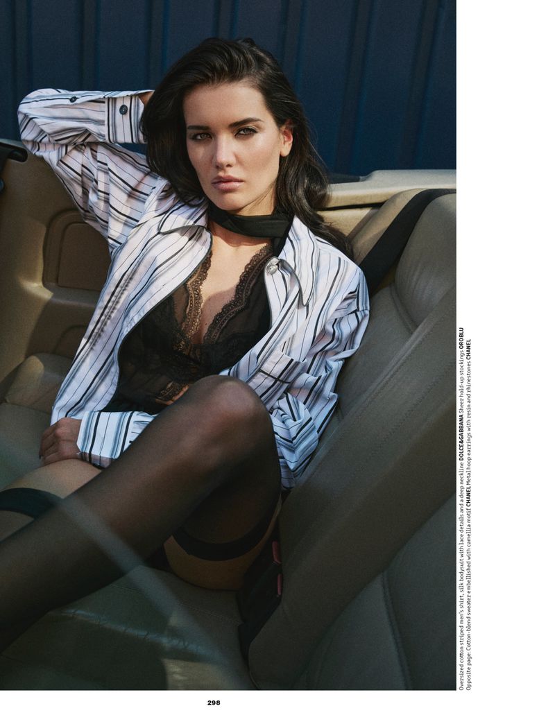 Woman in an unbuttoned striped shirt, black lace camisole, and sheer stockings reclining on leather car seats.