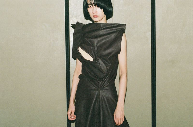 Model Asako Sato in a structured dark sleeveless draped dress posed before panelled walls for Vogue Philippines.