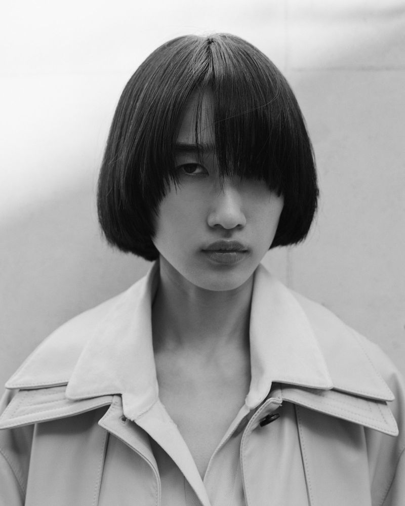 Black and white portrait of model Asako Sato with a blunt bob haircut wearing a wide-collar layered coat.