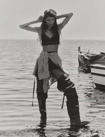 Black and white photo of Jennifer Matias standing in water wearing thigh-high rubber waders, a lace bra, and diving goggles on her head.