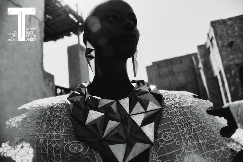 Black and white editorial portrait of a woman wearing a geometric faceted necklace and lace garment against architectural structures.