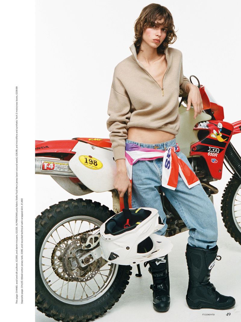 Mathilda Gvarliani posing in a beige half-zip and denim jeans beside a red dirt bike against a white background.