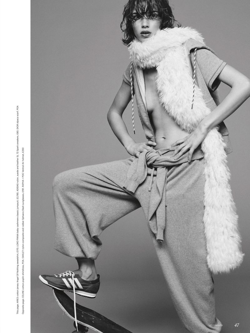 Model Mathilda Gvarliani posing with one foot on a skateboard in grey sweatpants and a fluffy white scarf against a grey backdrop.