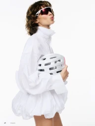 Model Mathilda Gvarliani in a voluminous white dress and shield sunglasses holding a white cycling helmet against a white background.