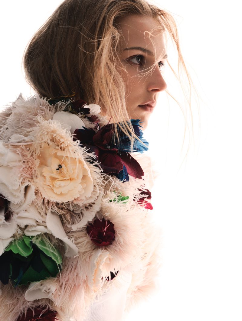 Valeria Buldini in profile wearing a heavily textured floral and feathered top against a high-key white background.