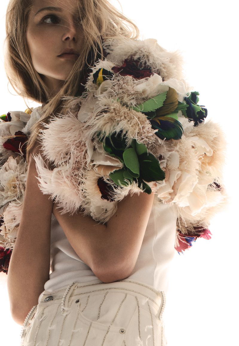 Model Valeria Buldini wearing an elaborate textured feather boa piece and embellished white denim against a bright white background.