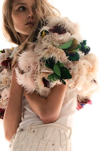 Model Valeria Buldini wearing an elaborate textured feather boa piece and embellished white denim against a bright white background.