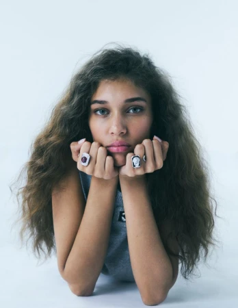Model Latahlia Hickling resting her chin on her fists wearing statement rings against a white backdrop.