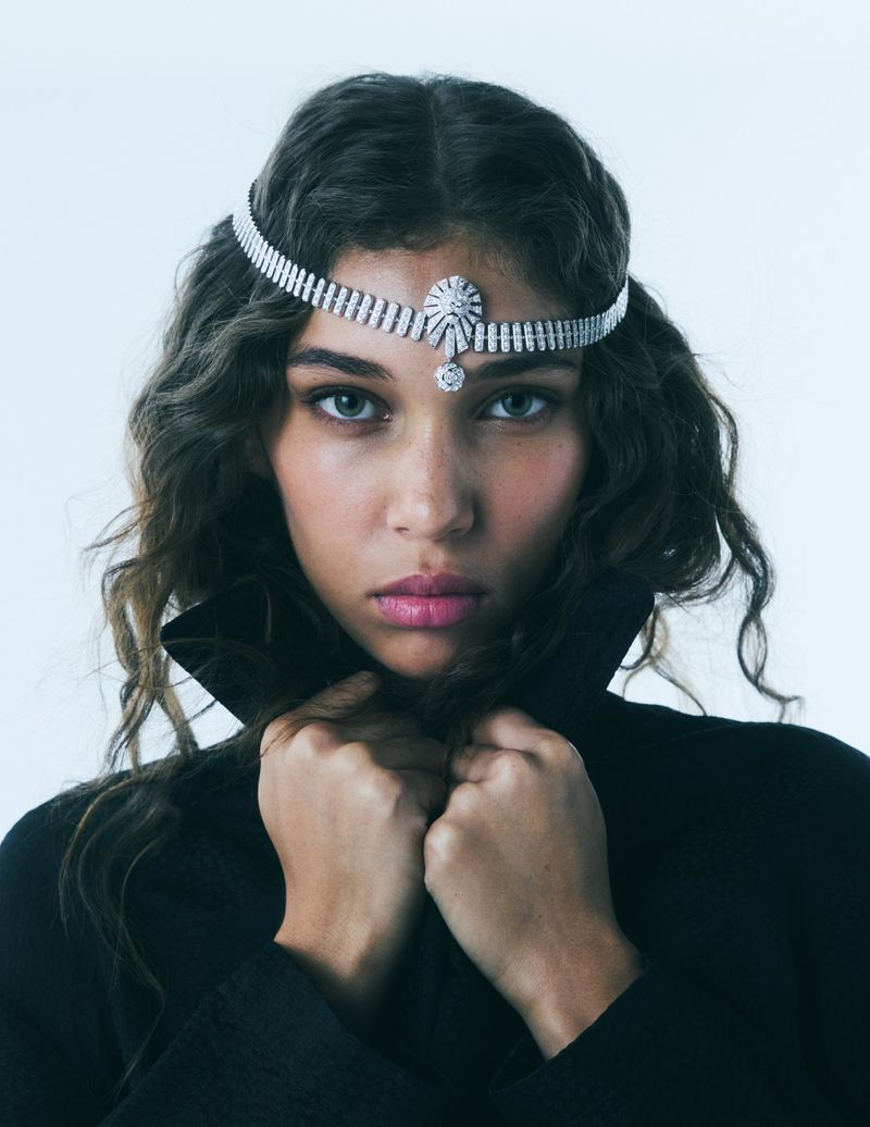 Model Latahlia Hickling wearing a diamond headpiece and high-collared black coat against a light studio backdrop.