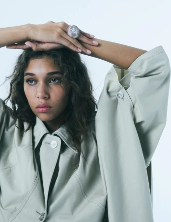 Model Latahlia Hickling wearing an oversized pale sage Chanel jacket and a large diamond dome ring against a plain studio background.