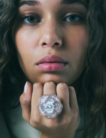 Close-up portrait of model Latahlia Hickling wearing a large diamond camellia ring by Chanel with hand under chin.