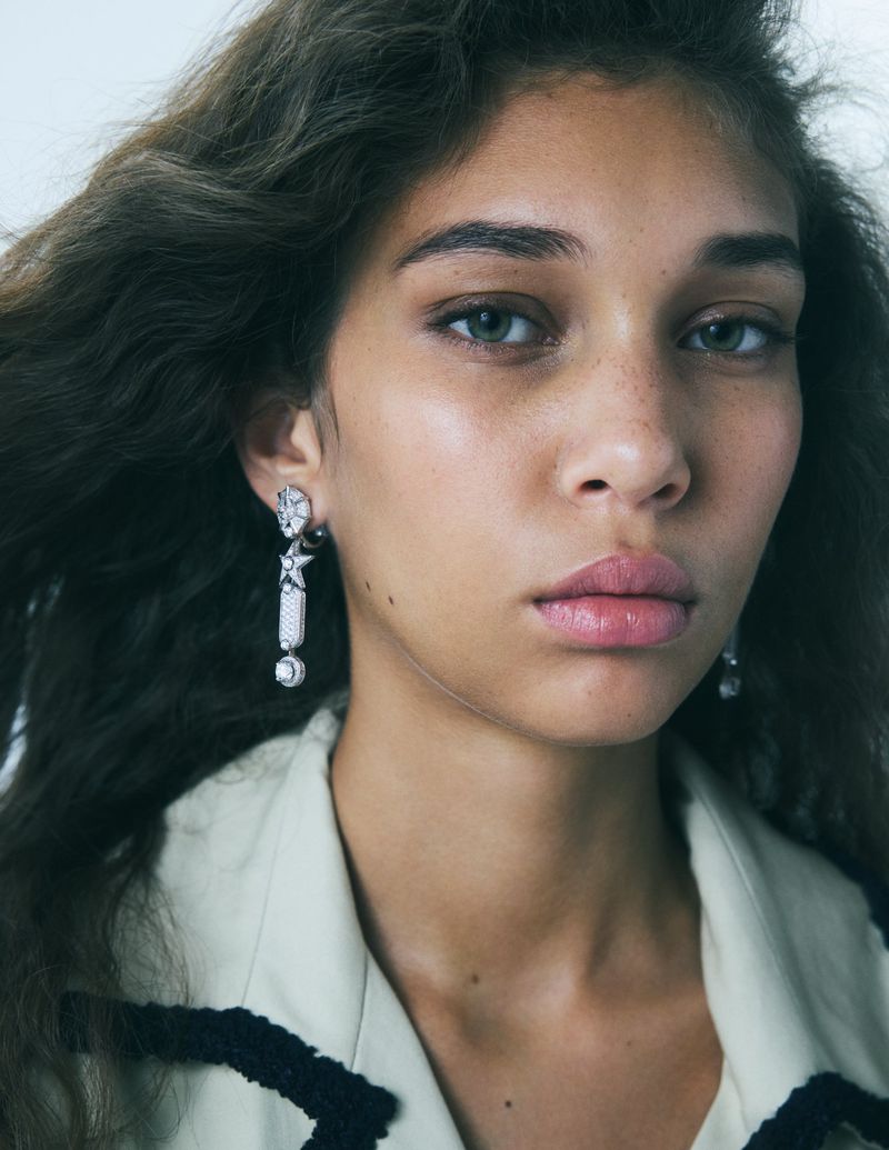 Close-up portrait of model Latahlia Hickling wearing geometric drop earrings and an off-white jacket with black trim.