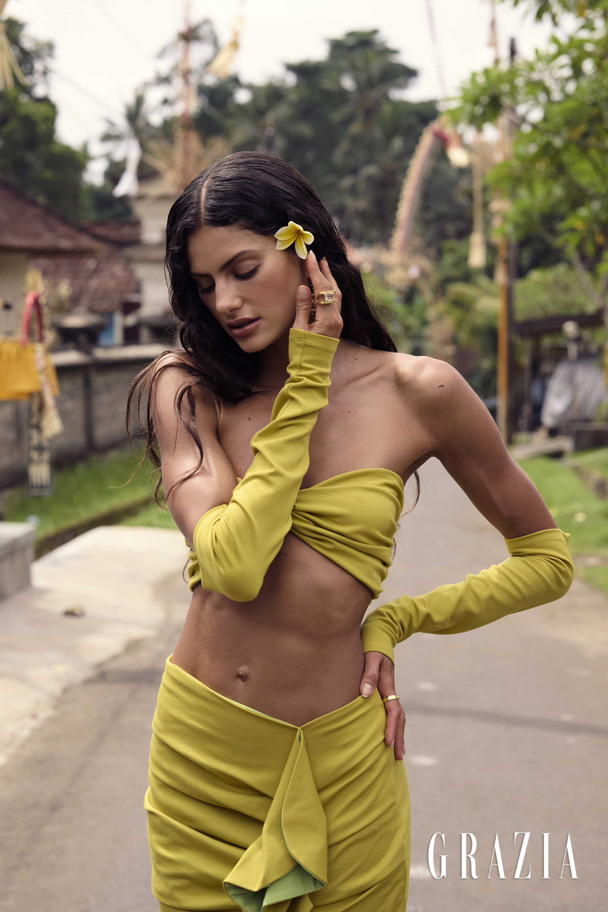 Woman in a chartreuse strapless two-piece set with matching sleeves and a yellow flower in her hair posing on a village road.