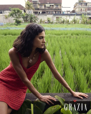 Model posing in a cream and pale yellow cut-out maxi dress outdoors among lush palm trees and tropical green rice terraces.