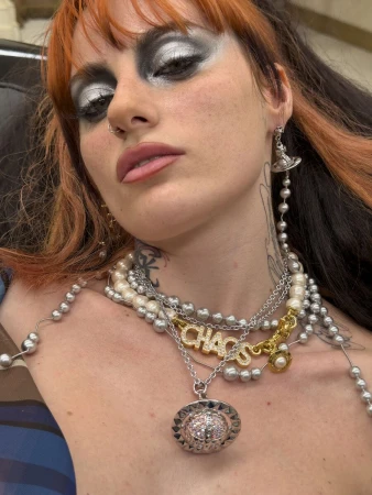 Close-up of a model with dramatic silver eye makeup wearing layered Vivienne Westwood pearl necklaces, CHAOS lettering, and orb pendant.