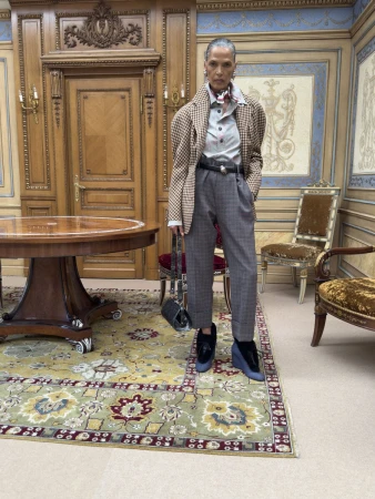 Model standing in an ornate paneled room wearing a checked blazer and grey trousers for Vivienne Westwood Fall 2026.