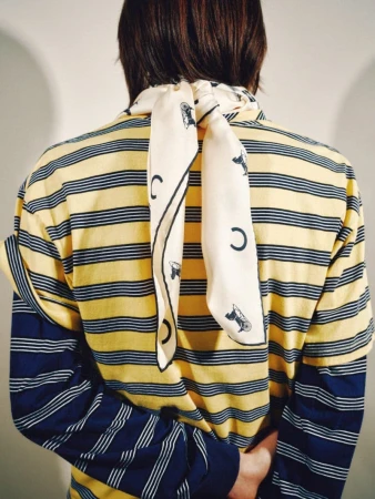 Person viewed from behind wearing layered yellow and navy striped shirts with a printed cream silk scarf knotted at the neck.