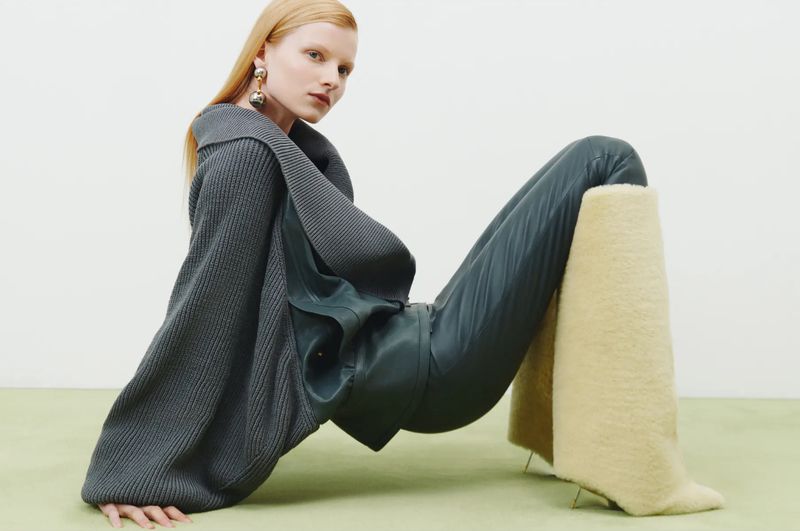 Fashion model in a grey sweater and leather pants poses in a studio with furry boots. Editorial fashion photography in a modern style.