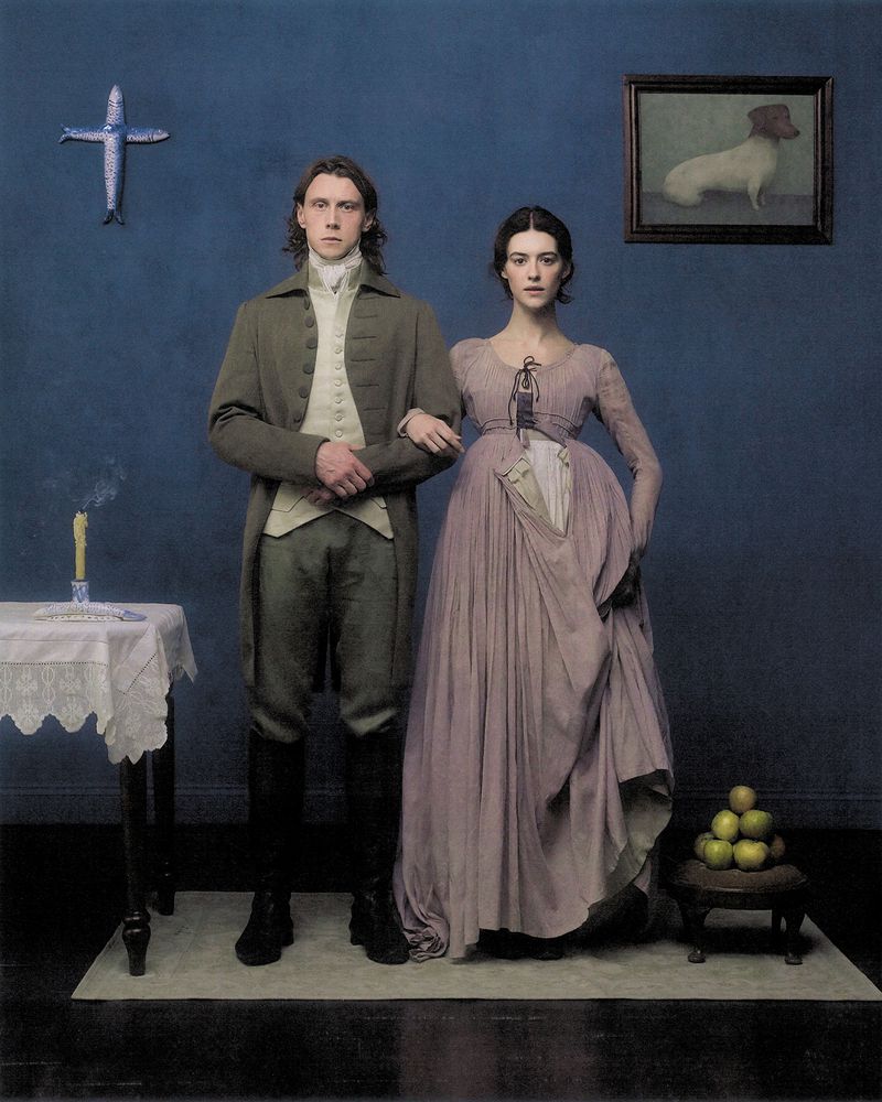Period portrait of George MacKay and Daisy Edgar-Jones standing against a dark blue wall for British Vogue