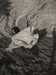 Model in motion wearing a ruffled white top and dark patterned skirt against a textured rock face.