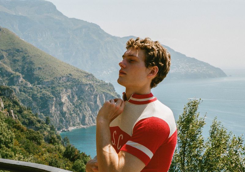 Caesar van den Idsert wearing a vintage red and cream cycling jersey against a coastal mountain backdrop.