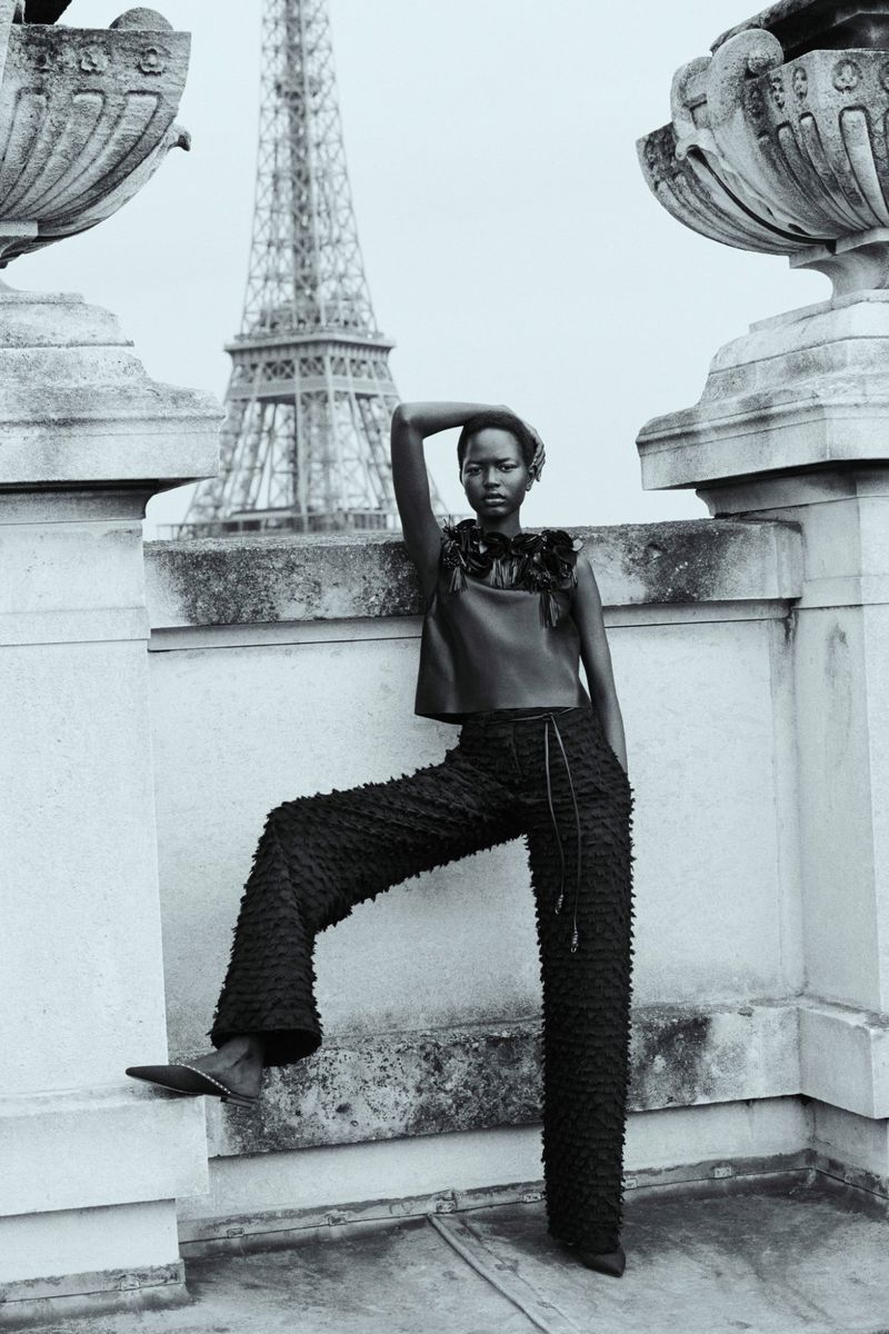 Black and white portrait of a model in Paris. She is wearing a dark, textured top and pants with the Eiffel Tower in the background.