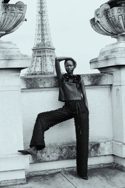 Black and white portrait of a model in Paris. She is wearing a dark, textured top and pants with the Eiffel Tower in the background.